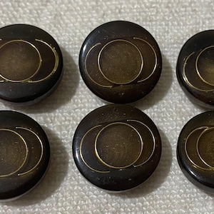 May include: Six dark brown, round buttons with a gold design. Each button has a central circle with two curved lines above and below. The buttons are arranged in two rows of three.