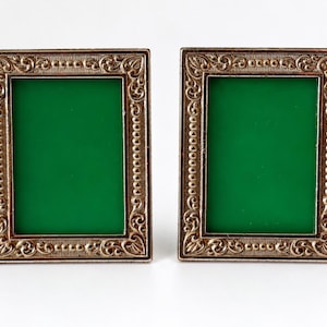 May include: Two rectangular picture frames featuring an ornate, metallic bronze-toned border with intricate scrollwork and bead detailing. Each frame contains a solid, vibrant green insert, creating a striking contrast against the metallic frame.