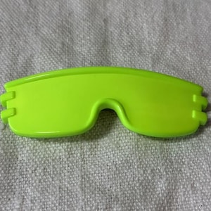 May include: A neon green, plastic eyewear frame, likely for sports or safety. The frame has a curved shape with a bridge for the nose and rectangular tabs on each end. The bright color suggests high visibility.