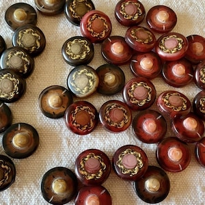 Puede incluir: Una colección de botones vintage en varios tonos de marrón, rojo y dorado. Los botones tienen forma de cúpula con diseños florales dorados y crema. Algunos botones tienen un centro rosa. Medidas no disponibles.