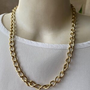 May include: A gold-colored chain necklace with large, interlocking oval links. The necklace is displayed on a white mannequin, showcasing its design and length. The chain is a classic jewelry piece.