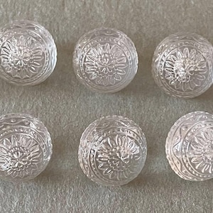 May include: Ten clear, spherical glass beads with a floral design. The beads are arranged in two rows of five, each bead showing intricate detailing. The beads are transparent, allowing light to pass through, and are suitable for jewelry making or crafts.