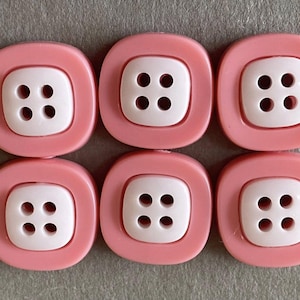 May include: Six square-shaped buttons with a pink border and a white center. Each button has four holes. The buttons are arranged in two rows of three.