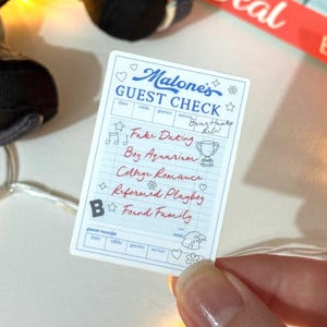 May include: A rectangular sticker featuring a blue and white guest check design titled Malone's Guest Check. The text includes Fake Dating, Boy Aquarium, College Romance, Reformed Playboy, and Found Family, decorated with stars, hearts, and a trophy.
