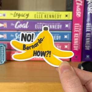 May include: A yellow banana sticker with the text "NO! Bernardo.. HOW?!" in black. The sticker is held in front of a bookshelf with books by Elle Kennedy.