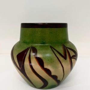 Può includere: Un vaso in ceramica verde con bordo marrone scuro e motivi astratti decorativi marroni e beige. Il vaso ha un corpo arrotondato e un collo leggermente svasato, adatto all'arredamento della casa.
