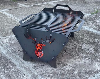 Pode incluir: Uma lareira de metal preto com um design de cabeça de veado recortada. A lareira tem uma grelha e alças. As chamas são visíveis no interior. A lareira está sobre uma superfície de concreto.