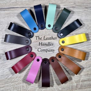 May include: A collection of colorful leather handles arranged in a circle. The handles come in various colors, including blue, black, green, yellow, and brown. Each handle is attached with a black rivet. The text "The Leather Handles Company" is also visible.