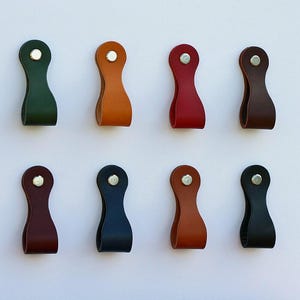 May include: Eight leather drawer pulls in various colors, including green, orange, red, and brown. Each pull has a loop design with a silver rivet at the top. The pulls are arranged in two rows of four against a white background.