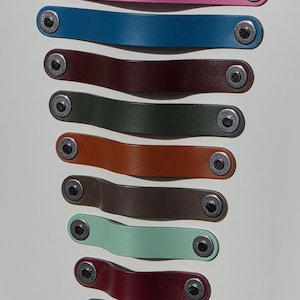 May include: A collection of colorful leather pull tabs in various shades, including yellow, brown, pink, blue, and red. Each tab is secured with a silver rivet. These tabs are likely for furniture or other decorative applications.