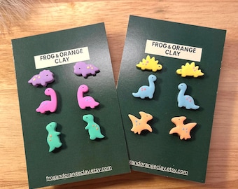 May include: Two dark green cards displaying colourful dinosaur-shaped clay figures. The cards feature the text "FROG & ORANGE CLAY" and the website address "frogandorangeclay.etsy.com". The dinosaurs are in shades of purple, pink, green, yellow, and orange.