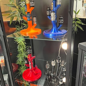 May include: A display case featuring colorful vape pen stands in orange, blue, red, and black. Each stand is designed to hold multiple vape pens, showcasing a variety of colors and styles. The stands are arranged on glass shelves.