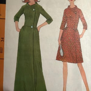 May include: Vintage sewing pattern featuring two women's dress designs. One dress is a long, olive green wrap dress with a button closure. The other is a shorter, red patterned dress with a similar button closure and three-quarter sleeves.