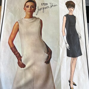 May include: Vintage Vogue Paris Original sewing pattern featuring a sleeveless dress design. The pattern includes a photograph of a woman wearing a cream-colored dress with pockets and a drawing of a black dress. The text "Vogue Paris Original" is at the top.