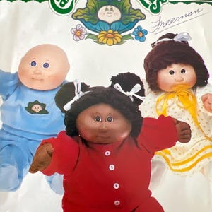 May include: A vintage Cabbage Patch Kids sewing pattern featuring three dolls. The dolls are wearing different outfits. The pattern is for a doll with brown hair, a doll with blonde hair, and a doll with black hair. The pattern is titled "Cabbage Patch Kids" and the number "6507" is printed on the top right corner.