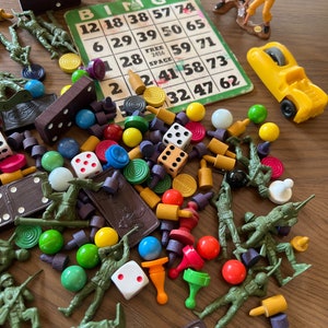 May include: A collection of vintage toys and games, including a bingo card, dominoes, dice, toy soldiers, and colorful game pieces. The bingo card has numbers and the word "BINGO" at the top.