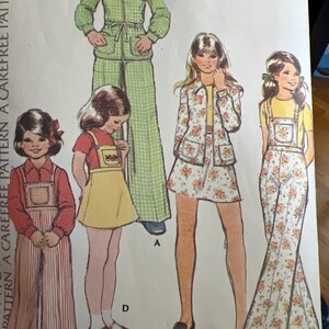 May include: A vintage sewing pattern featuring four different clothing designs for children. The pattern includes a green gingham jumpsuit, a floral print jacket and skirt, a striped overall dress, and a floral print overall dress. The pattern is labeled "Extra Carefree" and includes instructions for sizes 6-14.