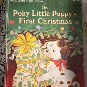 May include: A vintage children's book titled "The Poky Little Puppy's First Christmas." The cover features a puppy with brown spots and a red bow, holding a wrapped gift. The book has a green background with Christmas decorations.