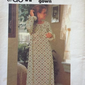 May include: A woman wearing a floral print lounging gown. The gown is long-sleeved with a tie at the neckline and ruffled cuffs. The text "SEW & GO" and "A pretty lounging gown" are visible at the top of the image.