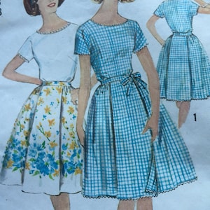 May include: Vintage sewing pattern featuring three illustrations of dresses. One dress is a white top with a floral skirt, and the other two are blue and white gingham dresses with short sleeves and a bow at the waist. The pattern is from the 1960s.