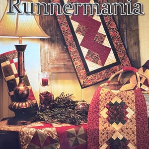 May include: The image showcases a collection of quilted table runners with a patchwork design. The runners feature a mix of burgundy, cream, and floral patterns. The text "Runnermania" is prominently displayed, suggesting a focus on table runner designs.