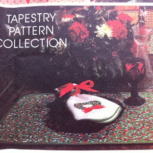 Pu&ograve; includere: Una collezione di motivi di arazzo con un design di agrifoglio rosso e verde. L'immagine mostra un sottopiatto con un tovagliolo bianco e un nastro rosso. Il testo "Tapestry Pattern Collection" &egrave; stampato sull'immagine.