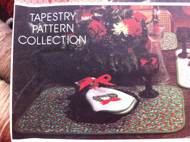 Pu&ograve; includere: Una collezione di motivi di arazzo con un design di agrifoglio rosso e verde. L'immagine mostra un sottopiatto con un tovagliolo bianco e un nastro rosso. Il testo "Tapestry Pattern Collection" &egrave; stampato sull'immagine.