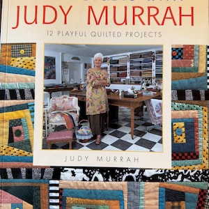 May include: A book cover titled "In The Studio With Judy Murrah" featuring a photo of Judy Murrah and examples of quilted projects. The cover has a yellow background with text and images of colorful quilts.