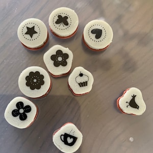 May include: Nine white rubber stamps with black ink designs. The designs include a star, a four-leaf clover, a heart, a flower, a cupcake, a bird, a flower, a coffee cup, and a flower.