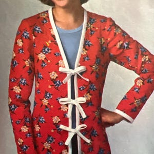 May include: A red floral print jacket with white trim and a white bow tie closure. The jacket has long sleeves and a V-neck.