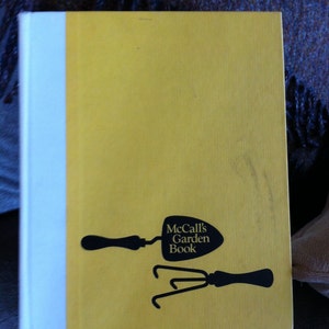 May include: A yellow book with a white spine. The book cover features a black silhouette of a trowel and a hand rake with the text "McCall's Garden Book".