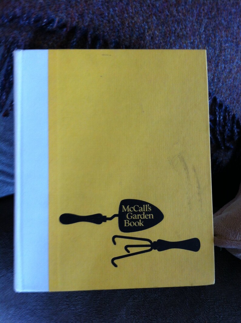 May include: A yellow book with a white spine. The book cover features a black silhouette of a trowel and a hand rake with the text "McCall's Garden Book".