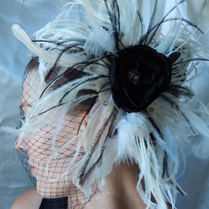 May include: A black flower with white feathers and rhinestones, worn as a hair accessory. The flower is made of fabric and has a satin finish.