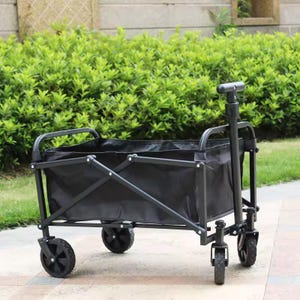 May include: A black folding utility wagon with a black fabric bed and a black metal frame. The wagon has four black wheels and a handle for pulling. The background features green foliage.