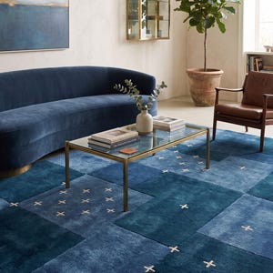 Puede incluir: Una alfombra rectangular grande con un diseño de patchwork en varios tonos de azul, incluyendo azul marino, azul real y verde azulado. La alfombra está decorada con un patrón repetitivo de pequeñas cruces bordadas de color claro.