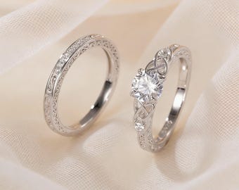 May include: Two silver rings. One is a band with a detailed pattern and small stones. The other ring has a large, round, clear stone and a Celtic knot design. Both rings are on a white background.