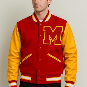 Puede incluir: Chaqueta universitaria roja y amarilla con una gran letra "M" en el pecho. La chaqueta tiene mangas de cuero amarillas, cuerpo rojo y puños y cuello a rayas blancas y amarillas. La chaqueta está abotonada.