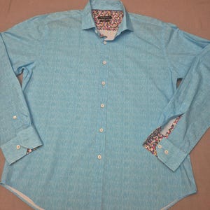 May include: A light blue long-sleeve button-down shirt. The shirt features a subtle textured pattern and a floral print lining the collar and cuffs. The shirt has a classic collar and buttoned cuffs.