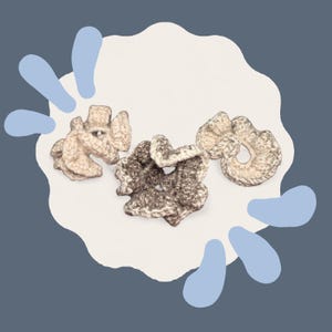 May include: Three handmade crochet scrunchies in shades of beige and brown, arranged on a white, cloud-shaped background. The scrunchies have a textured appearance, suggesting a soft, yarn-like material. The background is set against a dark blue backdrop with light blue accents.