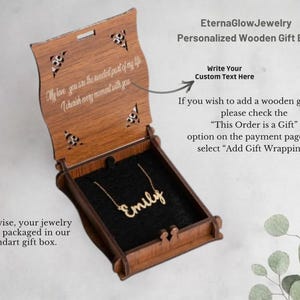 May include: A wooden gift box with a personalized necklace inside. The box is open, revealing a gold-colored necklace spelling "Emily" on a black velvet interior. The box has decorative cutouts and engraved text.