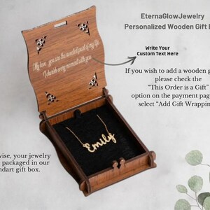 May include: A wooden gift box with a personalized necklace inside. The box is open, revealing a gold-coloured necklace spelling "Emily" on a black velvet interior. The box has decorative cutouts and engraved text.