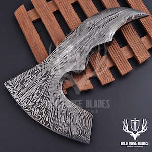 May include: A curved Damascus steel blade with a distinctive pattern. The blade is displayed on a wooden slatted surface. The text "WILD FORGE BLADES" and a logo are visible.