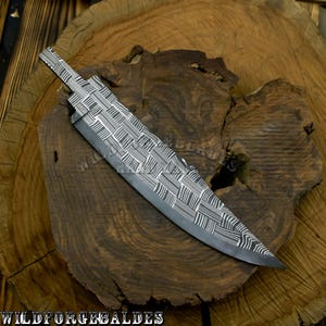 May include: A steel blade with a woven pattern design. The blade is dark gray with white accents and a pointed tip. The text "WILDFORGEBALDES" is at the bottom of the image.