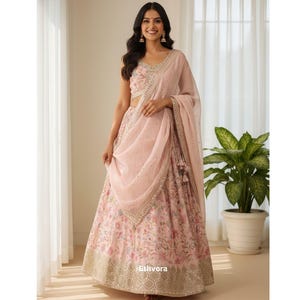 May include: A light pink floral print lehenga choli set with a matching dupatta. The set features intricate embroidery and embellishments. The dupatta is draped over the shoulder. The outfit is suitable for festive occasions.