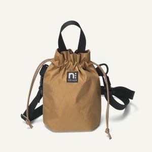 May include: A tan drawstring bucket bag with a black handle and shoulder strap. The bag has a small square label with the letter "n" and the word "постился" printed on it. The bag is made of a lightweight material.