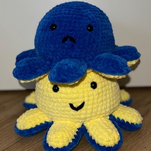 May include: A handmade, reversible crochet octopus plushie. One side is yellow with a smiling face and blue accents, the other is blue with a sad face. The plushie is soft and cuddly, perfect for children or as a decorative item.