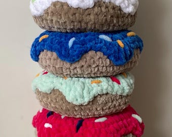 Puede incluir: Una pila de seis donuts de ganchillo con glaseado y chispas de colores. Los donuts tienen bases marrones y están cubiertos con glaseado rosa, blanco, azul, verde, rojo y amarillo. Un postre hecho a mano.