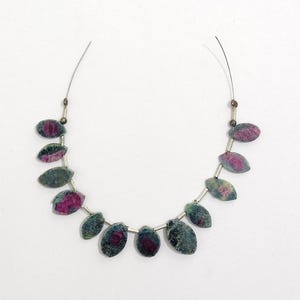 May include: A necklace featuring oval-shaped beads with a mix of colors. The beads have a dark green and gray base with a vibrant pink center. The beads are strung on a silver wire.
