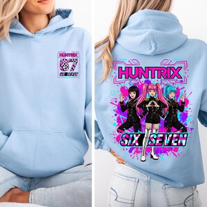 May include: Light blue hoodie with a front pocket and a graphic on the front and back. The front graphic says "HUNTRIX 67 SIX SEVEN". The back graphic features three anime-style characters with the text "HUNTRIX SIX SEVEN" in a neon design.