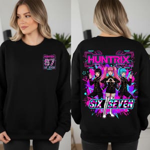 May include: Black sweatshirt with the text "HUNTRIX" and "SIX SEVEN" in a neon pink and blue design. The front features a small logo, while the back displays a graphic of three anime-style characters.